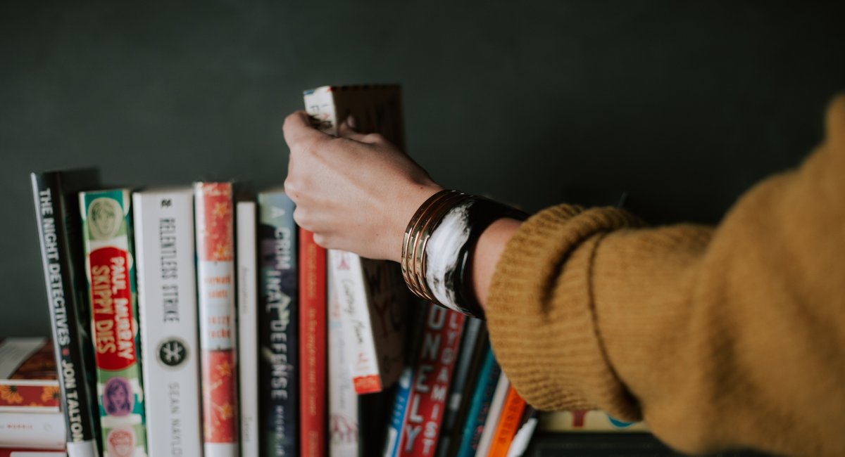 Person picking white and red book on bookshelf