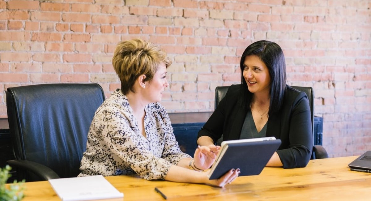 Let me ask you one more thing about that. Two businesswomen talking at a desk with a tablet in hand