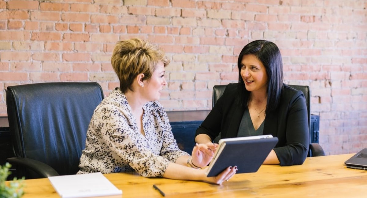 Two businesswomen talking at a desk with a tablet in hand