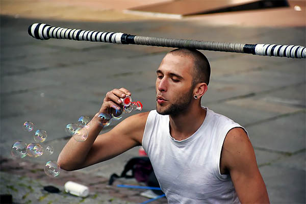 Man blowing bubbles while balancing a pole on his head