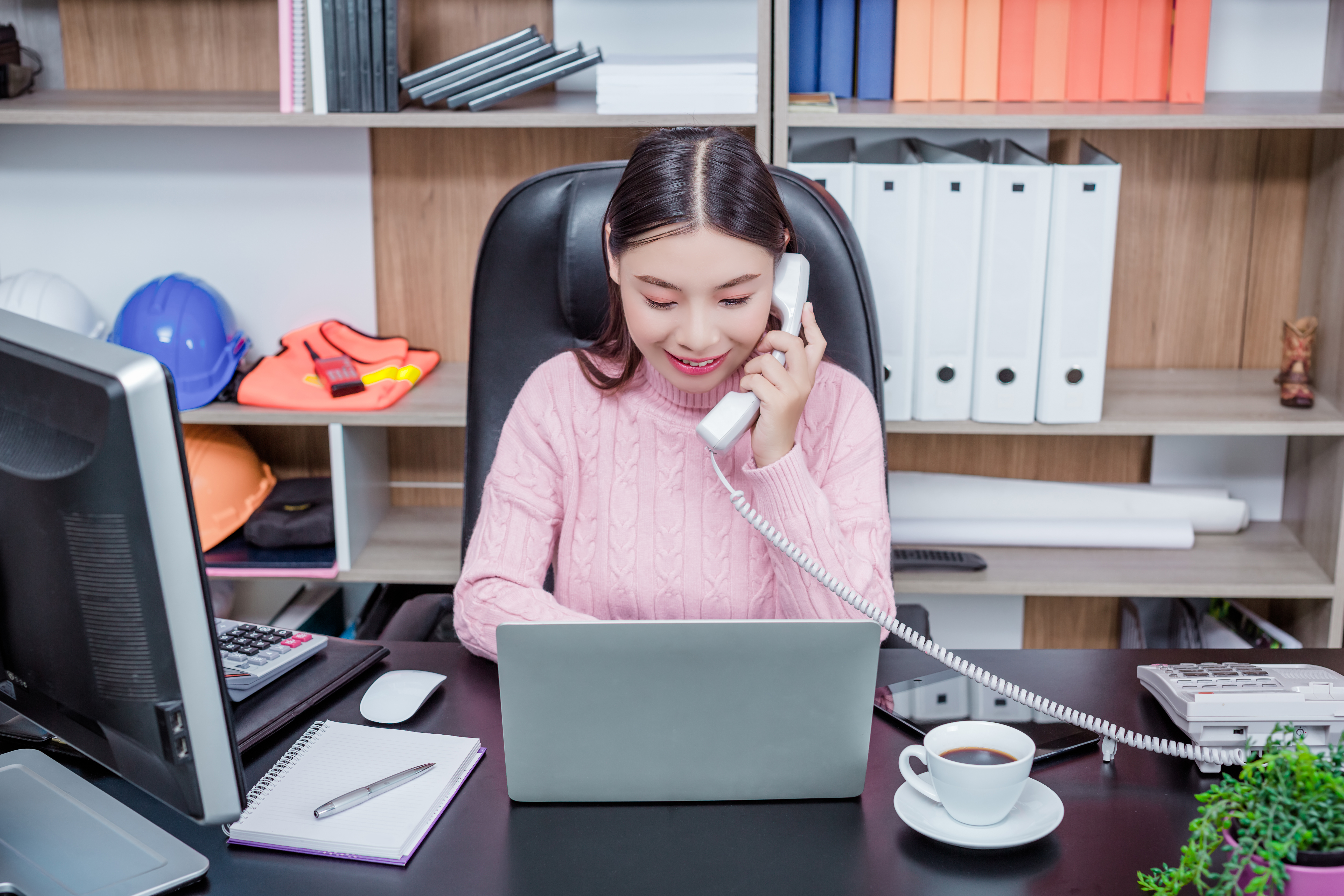 Young woman talking on the phone in her office in front of a laptop computer