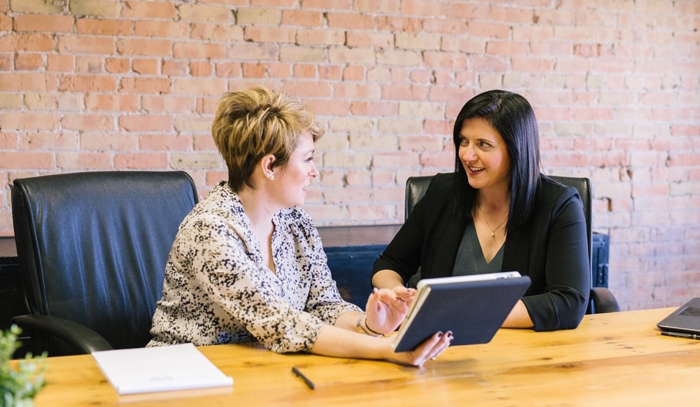 Two businesswomen talking at a desk with a tablet in hand