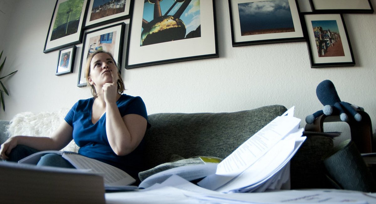 Woman sitting on a couch with papers strewn about, trying to think of something