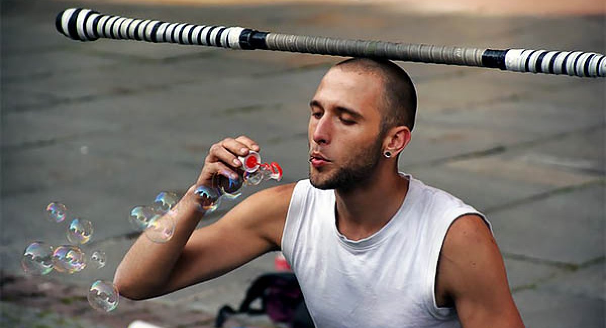 Man blowing bubbles while balancing a pole on his head
