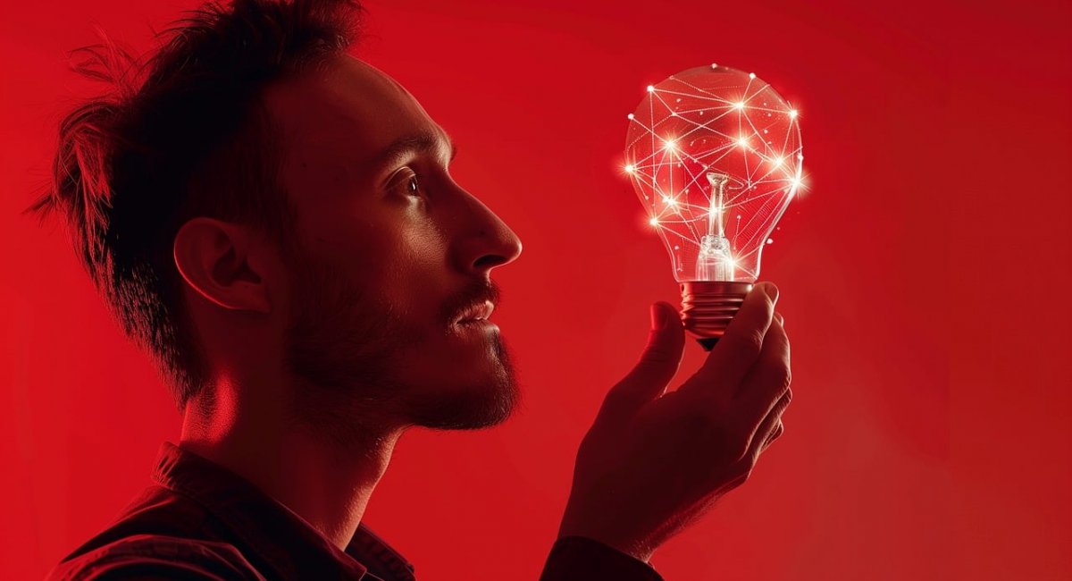 A bearded man looks at a lightbulb he is holding. The bulb is filled with bright connections. 